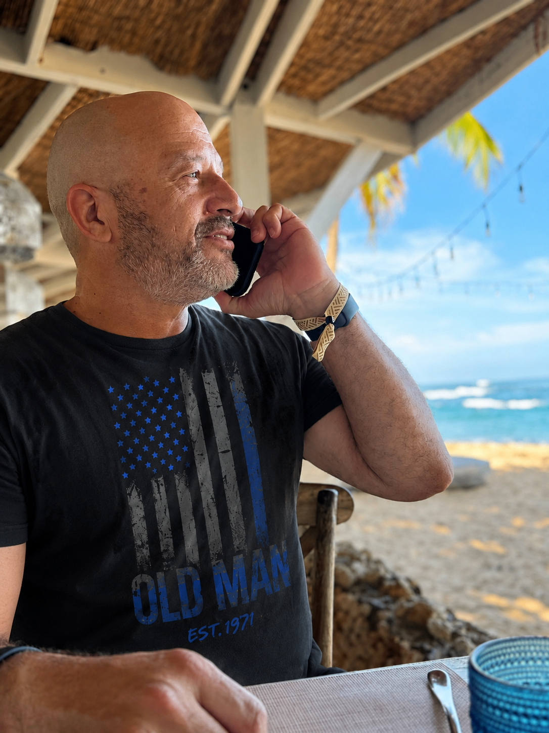 Man wearing a black custom t-shirt with blue flag artwork while on the phone.